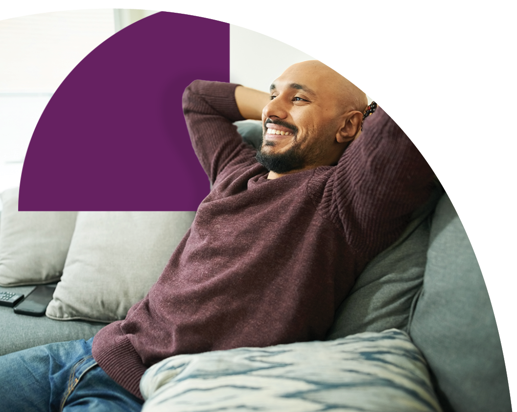 Happy young man relaxing on sofa in living room with phone near by knowing his deposits are safe with Saven Financial.